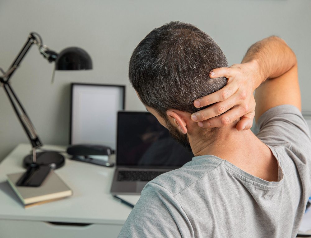 Persona con dolor de cuello en su puesto de trabajo frente al ordenador