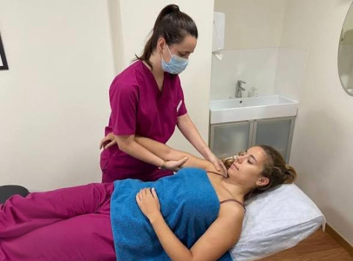 Fisioterapeuta realizando una movilización pasiva del hombro a una paciente tumbada en una camilla.