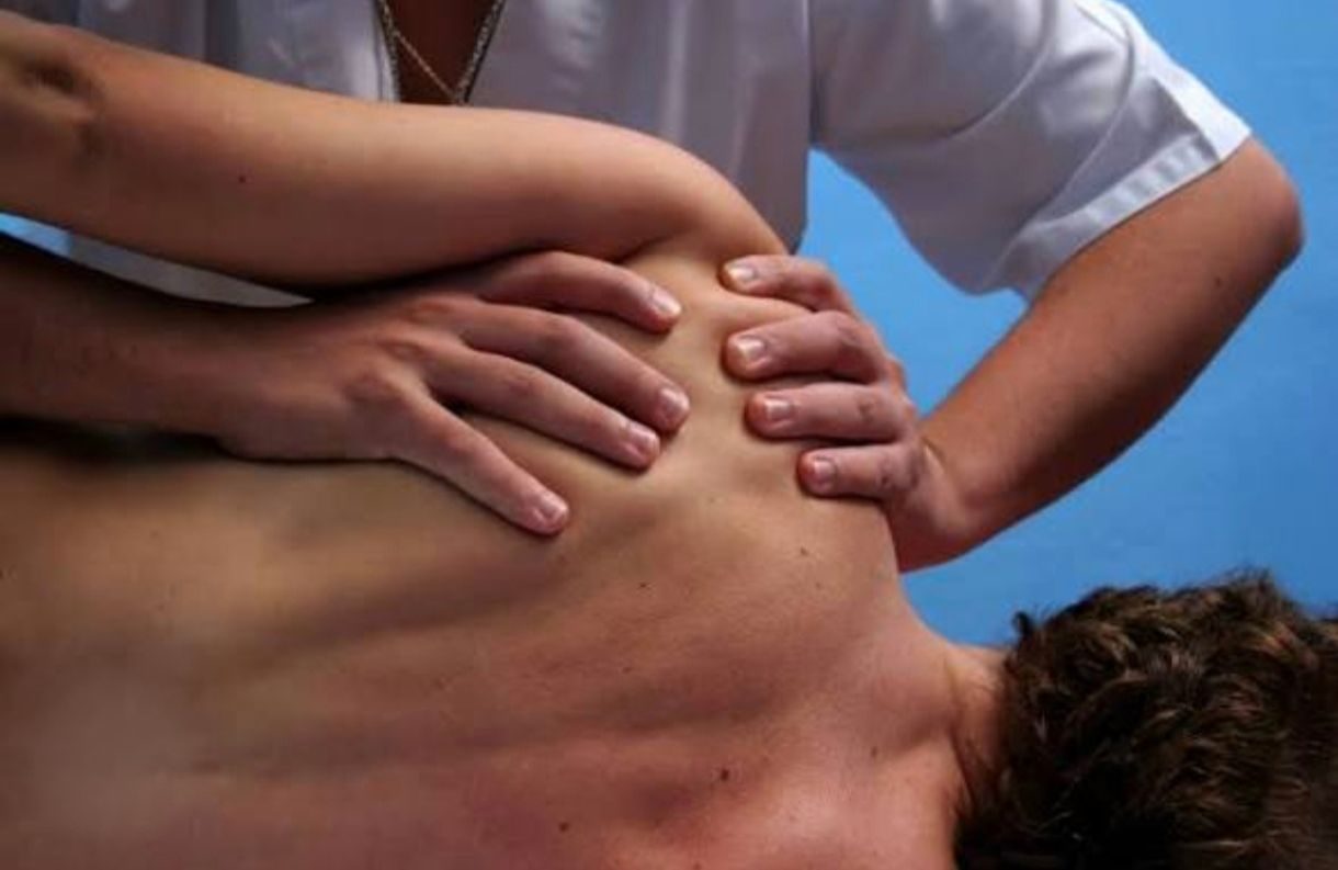 Fisioterapeuta aplicando técnicas de terapia manual en la zona del hombro y la escápula de un paciente.