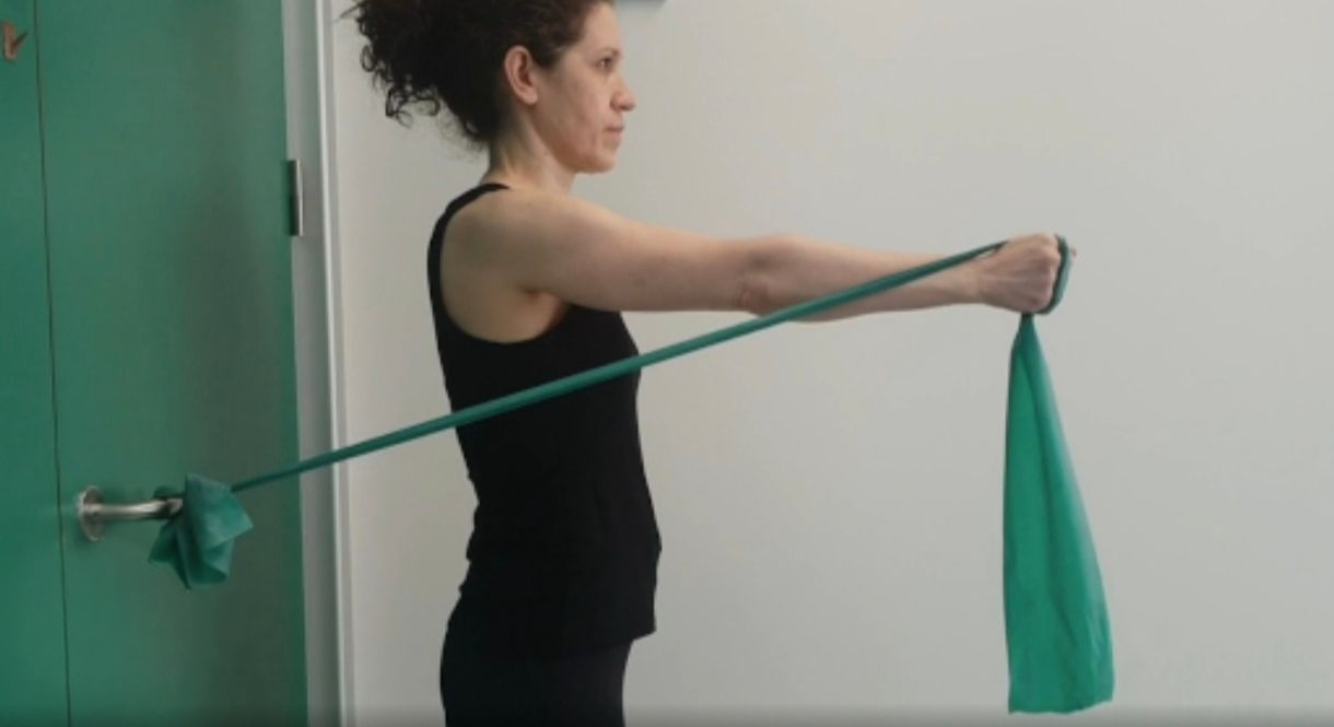 Mujer realizando un ejercicio de fortalecimiento del hombro con banda elástica como parte de su rehabilitación.
